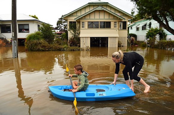 Binti Jones and her son Matthew, 5, paddles along a flooded street towards their home in Lismore on Saturday.