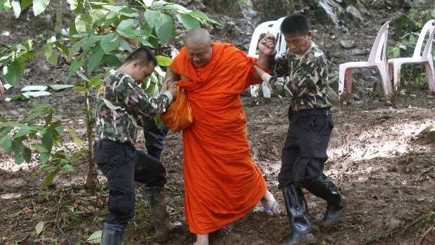 A Buddhist monk, helped by Thai rescues, walks after praying near the cave complex where the 12 boys and their soccer coach went missing.