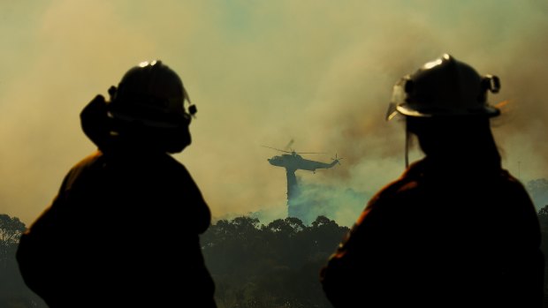 RFS crew members watch a helicopter dropping water on the fire front at Barden Ridge, Sydney.