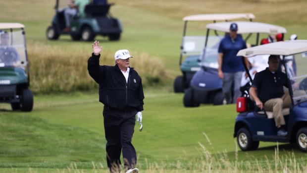President Donald Trump waves to protesters while playing golf in Scotland.