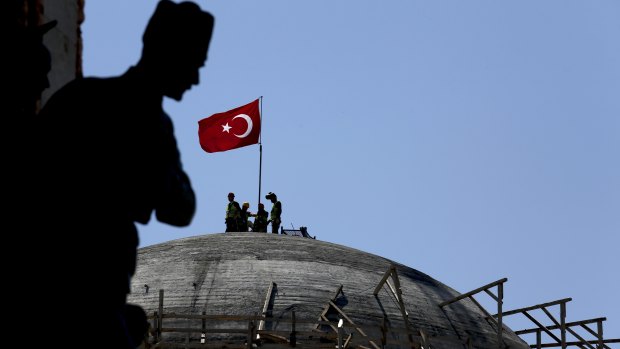 A sculpture of Turkey's founder Kemal Attaturk, sits on the monument of the Republic, as construction workers beyond place a Turkish national flag on the dome of the under-construction mosque in Taksim square in Istanbul.