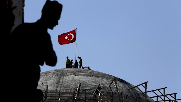 A sculpture of Turkey's founder Kemal Attaturk, sits on the monument of the Republic, as construction workers beyond place a Turkish national flag on the dome of the under-construction mosque in Taksim square in Istanbul.