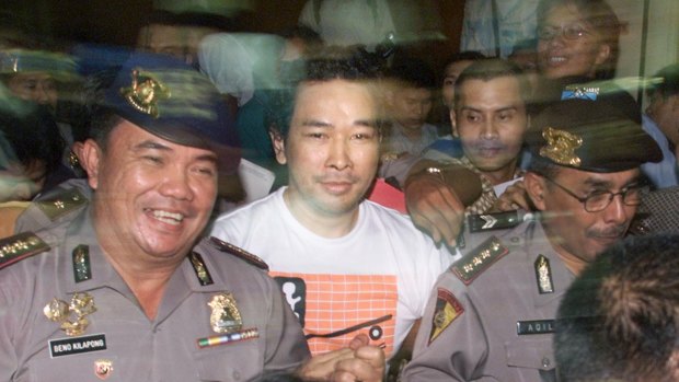 A police officer, left, smiles as he escorts Tommy, fugitive son of former Indonesian President Suharto, through a mob of reporters after his capture at police headquarters in Jakarta, Indonesia.