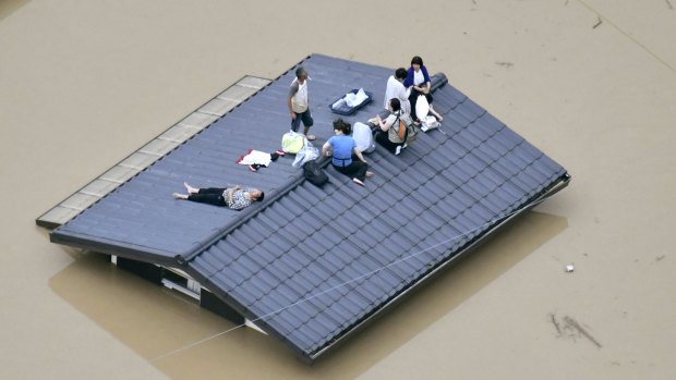 Stranded people waiting to be rescued on the top of a house almost submerged in the floodwaters.