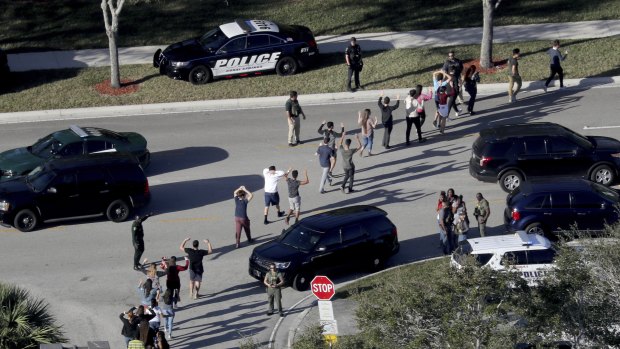 Students hold their hands in the air as they are evacuated by police from Marjory Stoneman Douglas High School.
