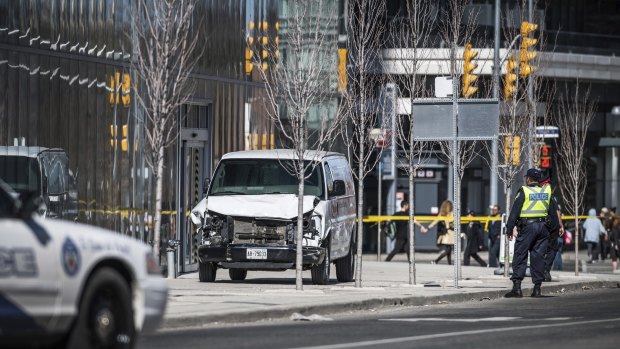 Toronto police officers stand near a damaged van after it  mounted a sidewalk crashing into pedestrians in Toronto.