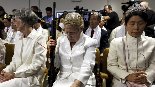 A woman wears a crown and holds an unloaded weapon as she bows her head during services at the World Peace and Unification Sanctuary, in Newfoundland, Pennsylvania.