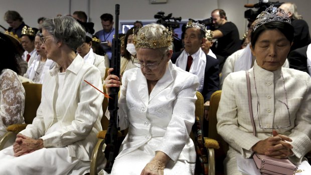 A woman wears a crown and holds an unloaded weapon as she bows her head during services at the World Peace and Unification Sanctuary, in Newfoundland, Pennsylvania.