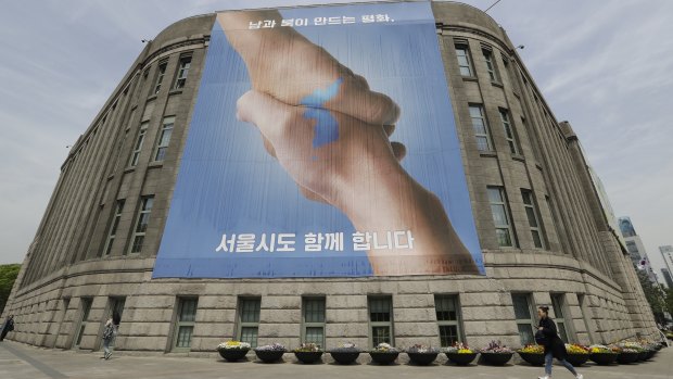 A woman walks by a Seoul banner showing a map of the Korean peninsula and a message for a successful inter-Korean summit.