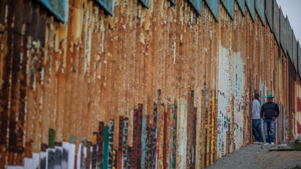 A person looks through a section of a US-Mexico border wall in Tijuana, Mexico.