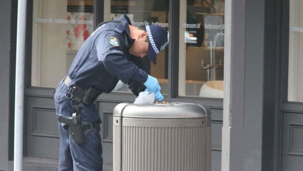 A police officer searches bins near the site of the explosion in Rozelle.