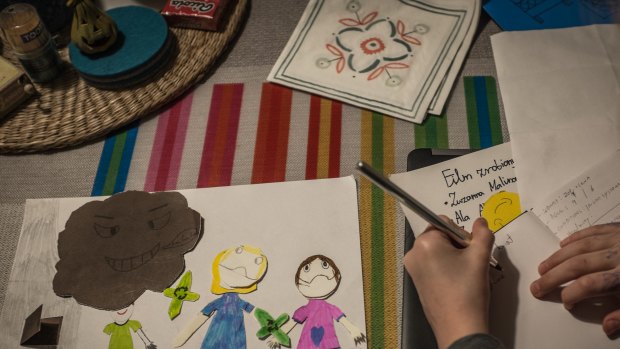 Zoe writes on a notebook beside one of her drawings of her family.