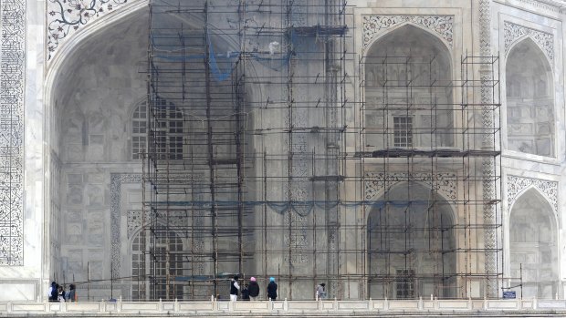 Tourists walk past a discoloured wall of the Taj Mahal caused by environmental pollution, which stands out in contrast against one that has been cleaned.
