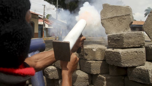 An anti-government protester fires a homemade mortar at the police from a barricade. 