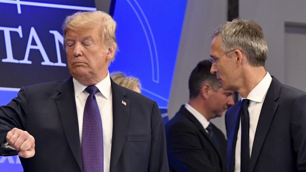 Donald Trump checks the time as Jens Stoltenberg stands beside him, in Brussels.