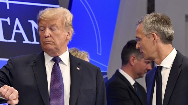 Donald Trump checks the time as Jens Stoltenberg stands beside him, in Brussels.