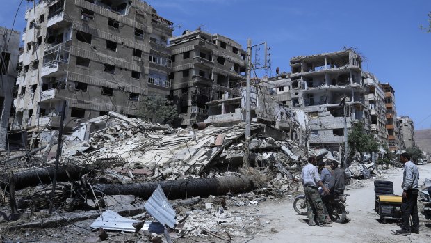 People stand in front of damaged buildings, in the town of Douma, the site of a suspected chemical weapons attack, near Damascus, Syria.