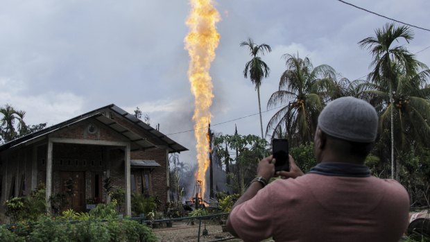 A man takes photos of a burning oil well after it caught fire in Pasir Putih village in eastern Aceh, Indonesia.