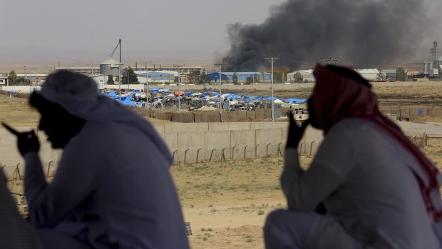 Jordanian residents of Jabir village watch aid deliveries to Syrians fleeing the government offensive in the south as smoke from unknown fire rises.