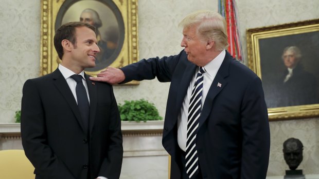 President Donald Trump playfully reaches over to clean "dandruff" or lint off French President Emmanuel Macron.