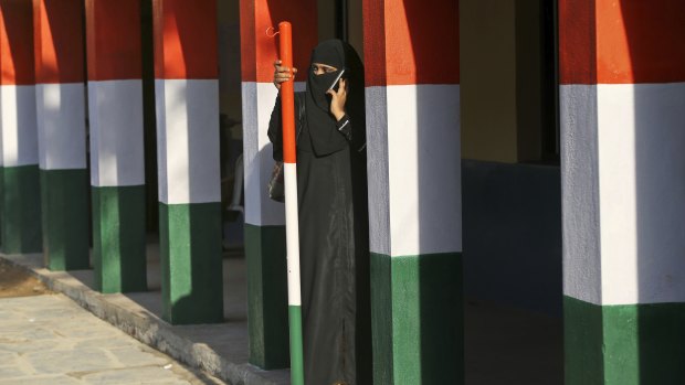 A Muslim woman talks on her mobile phone as she stands between pillars painted in the colours of the Indian national flag after casting her vote at a polling station in Bangalore.