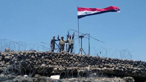 Syrian troops flash the victory sign next to the Syrian flag in Tell al-Haara, the highest hill in the southwestern Daraa province, Syria. 
