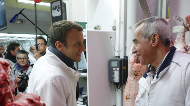 Then French presidential candidate Emmanuel Macron, left, shakes hands with a butcher as he visits the meat pavillion at the Rungis wholesale food market, south of Paris, in May 2017. 