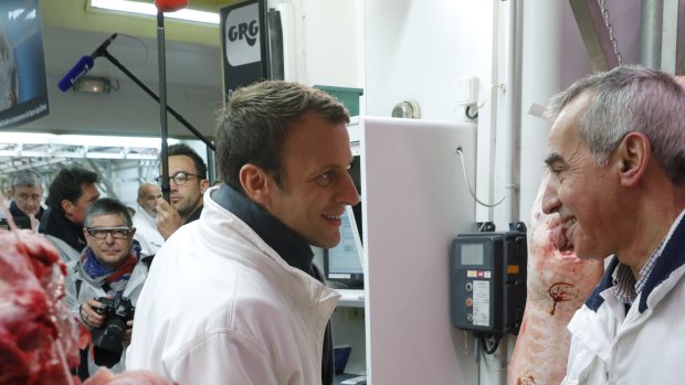 Then French presidential candidate Emmanuel Macron, left, shakes hands with a butcher as he visits the meat pavillion at the Rungis wholesale food market, south of Paris, in May 2017. 