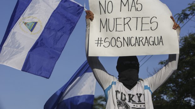 A masked demonstrator holds a Nicaraguan flag and a sign with a message that reads in Spanish: "No more deaths".