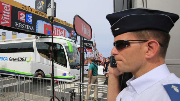 A French gendarme talks on his communication equipment while a man lets the air out of the tyre of the Orica GreenEDGE cycling team bus after it got stuck on the finish line of the first stage of the Tour de France.