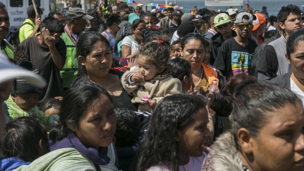 Families from a caravan of migrants from Central America who travelled through Mexico wait for a meal near the US border wall in Tijuana.