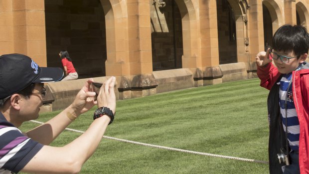 A man forming part of a Chinese tour group takes a photo of his son at the University of Sydney.