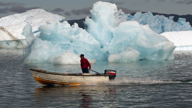 A fisherman sails past melting icebergs in Greenland,