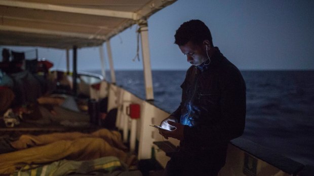 A migrant checks his phone as other sleep on the deck of the Open Arms aid boat, of Proactiva Open Arms Spanish NGO after being rescued from a rubber dinghy off the Libyan coast on July 1.