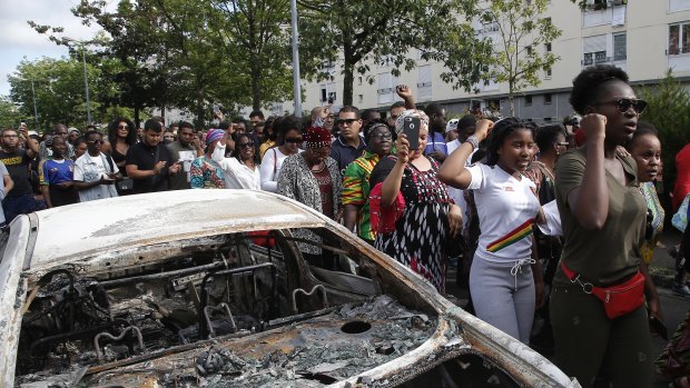 People walk past a charred car during a march after police shot of a driver.