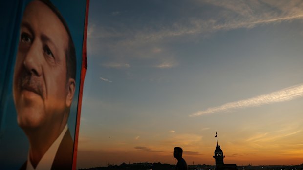 Backdropped by the Bosporus Strait separating Asia and Europe, a man strolls past an election poster of President Recep Tayyip Erdogan, in Istanbul.