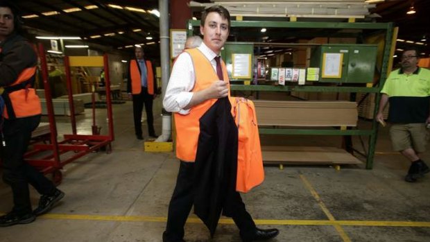 Opposition Leader Tony Abbott's jacket is carried by a staffer during his tour of a door manufacturer in Western Sydney