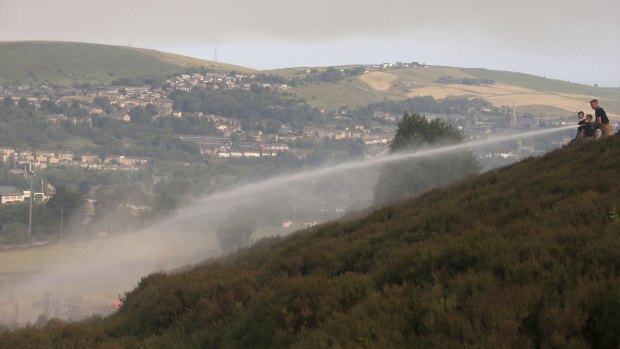 Firefighters work to damp-down land on Saddleworth Moor as a wildfire threatens a nearby village.