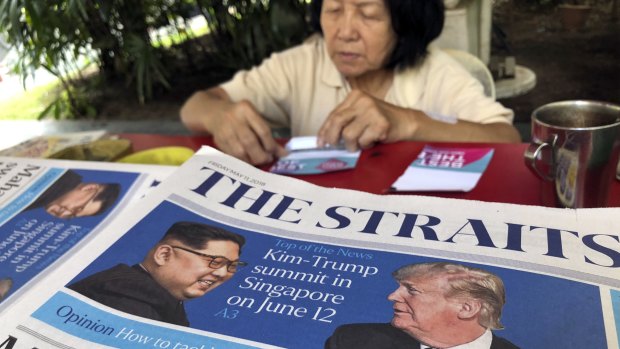 A news vendor counts her money near a stack of newspapers with a photo of Trump, right, and Kim on its front page in Singapore. 