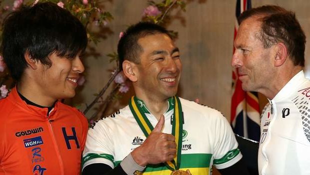 Minori Shinmura and Kouji Yoshii, cyclists from the Japan Cycling Federation, shows his gold medal to Prime Minister Tony Abbott ahead of their bike ride, in Tokyo on Sunday 6 April 2014.