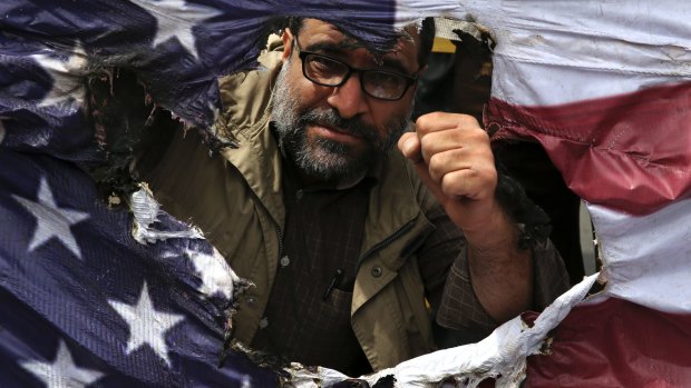 An Iranian protester clenches his fist behind a burnt representation of the US flag in Tehran.