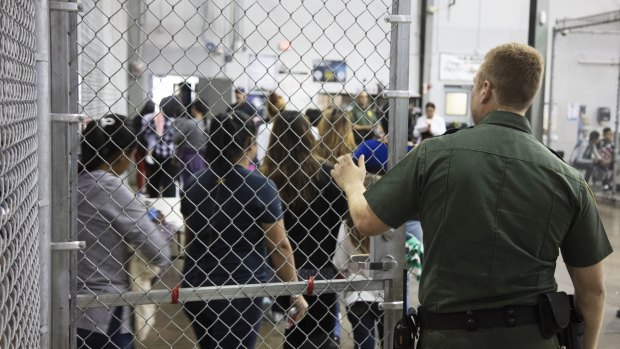 A US Border Patrol agent watches as people who\'ve been taken into custody related to cases of illegal entry into the United States, stand in line at a facility in McAllen, Texas.