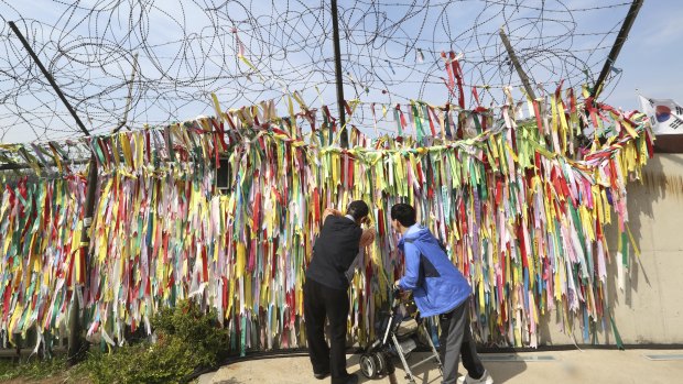 A man hangs a ribbon carrying messages wishing the reunification and peace of the two Koreas on the wire fence near the border.