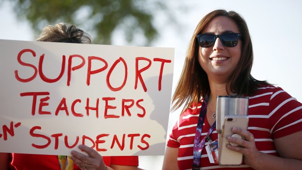Stefanie Lowe, a teacher at Tuscano Elementary School, smiles as she joins other teachers, parents and students as they stage a "walk-in" for higher pay and school funding in Phoenix. 