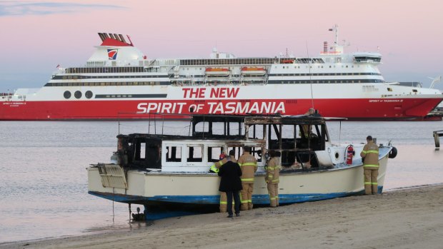 Boat badly damaged by fire on Port Melbourne beach this morning is inspected by firemen and police.