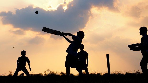 Boys play cricket against a cloudy sunset in India.