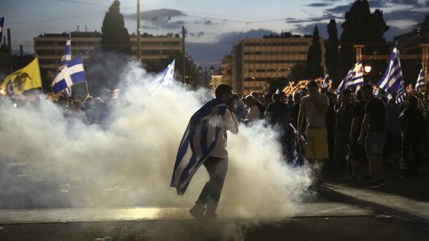 A protester with a Greek flag walks through smoke of a tear gas canister thrown by riot police during a demonstration against the agreement between Greece and Macedonia in Athens on Saturday.
