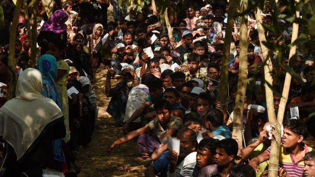 Rohingya refugees sit in a queue at a Red Cross distribution point in Burma Para refugee camp.