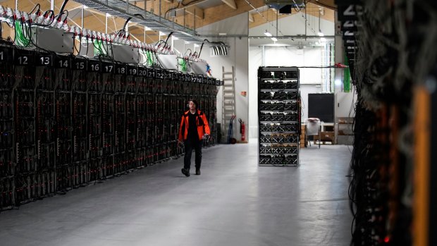 A worker walks along a row of computer rigs that run around the clock 'mining' bitcoin inside the Genesis Mining cryptocurrency mine in Keflavik, Iceland. 