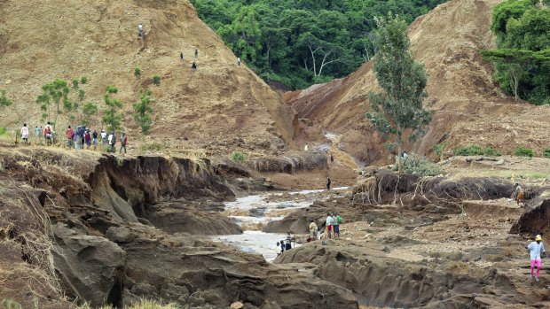 People gather in front of the broken banks of the Patel dam near Solai.